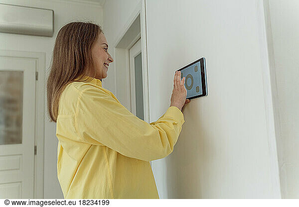 Smiling woman using tablet PC mounted on white wall at home