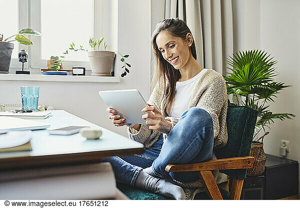 Smiling woman using tablet PC sitting on chair at home