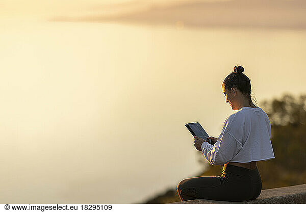 Smiling woman using tablet PC sitting on wall