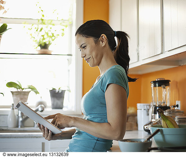Smiling woman using tablet while standing at kitchen counter in home
