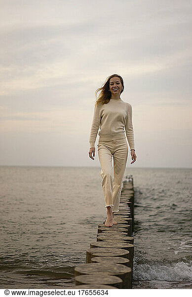 Smiling woman walking on wooden post at beach