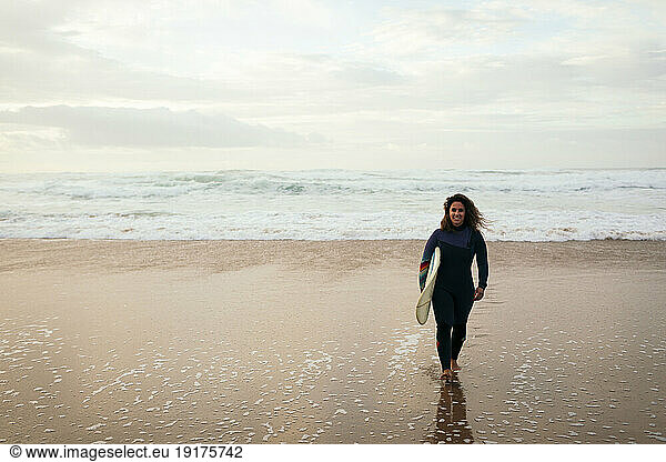 Smiling woman walking with surfboard at beach