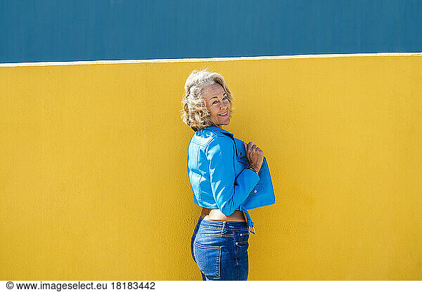 Smiling woman wearing blue leather jacket in front of wall