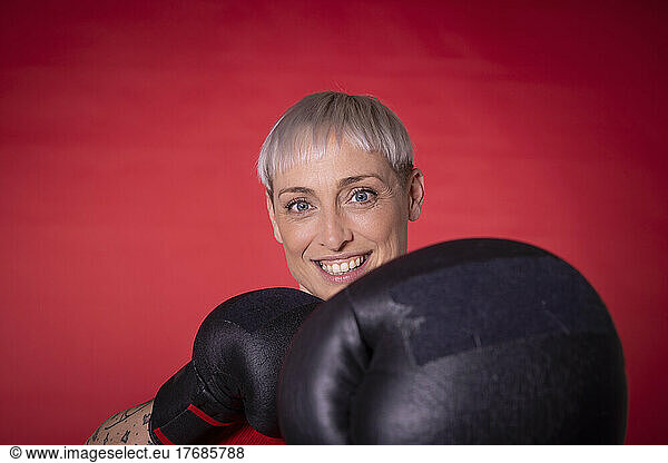 Smiling woman wearing boxing gloves against red background