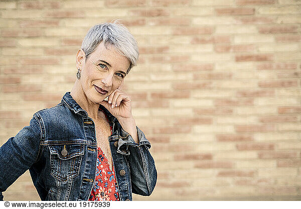 Smiling woman wearing denim jacket standing in front of wall
