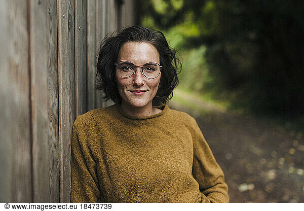 Smiling woman wearing eyeglasses leaning on wooden wall