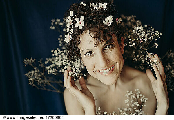 Smiling woman wearing flowers against blue background