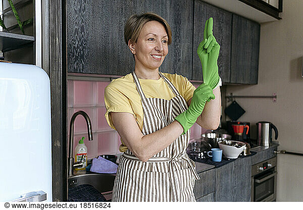 Smiling woman wearing gloves standing in kitchen