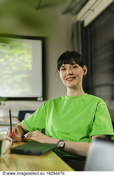 Smiling woman wearing green t-shirt sitting in office conference room