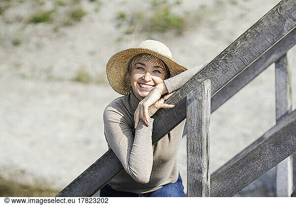 Smiling woman wearing hat leaning on railing