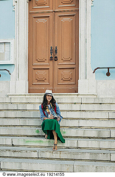 Smiling woman wearing hat sitting on steps in front of door