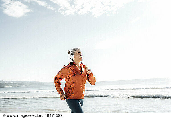 Smiling woman wearing headphones jogging at beach