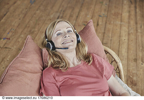 Smiling woman wearing headset lying on cushions at home