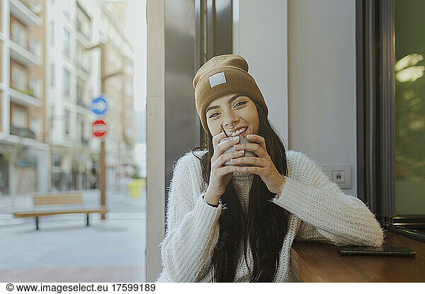 Smiling woman wearing knit hat sitting at sidewalk cafe