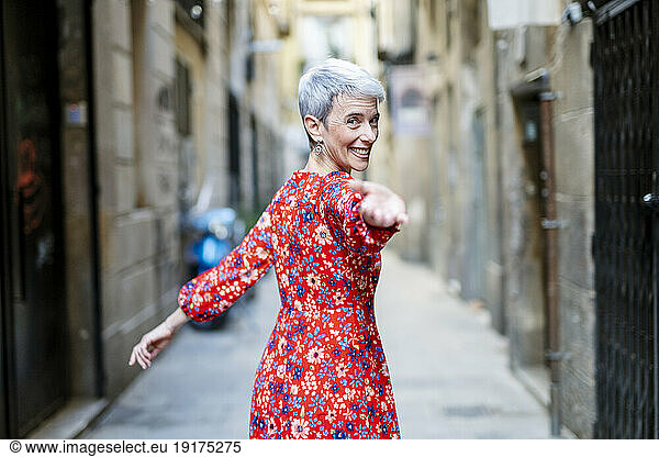 Smiling woman wearing red dress beckoning in alley