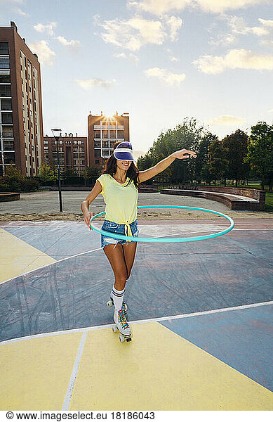 Smiling woman wearing roller skates dancing with hoop at sports court