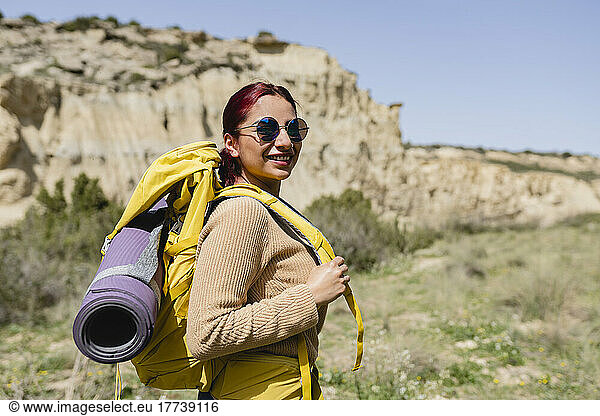 Smiling woman wearing sunglasses and backpack on sunny day