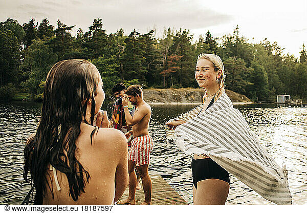 Smiling woman wearing towel while looking at female friend during vacation