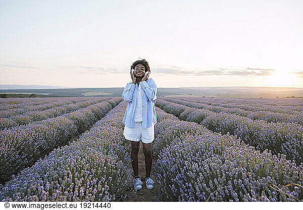 Smiling woman wearing wireless headphones in lavender field