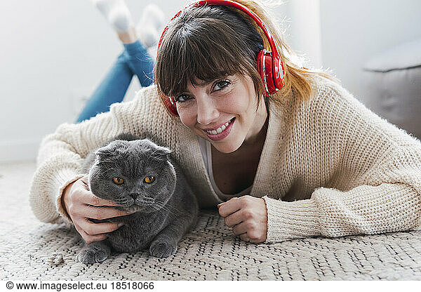 Smiling woman wearing wireless headphones lying down with cat at home