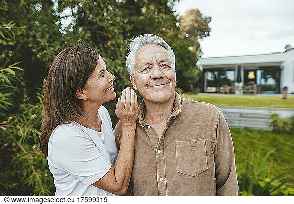 Smiling woman whispering in senior man's ear at backyard