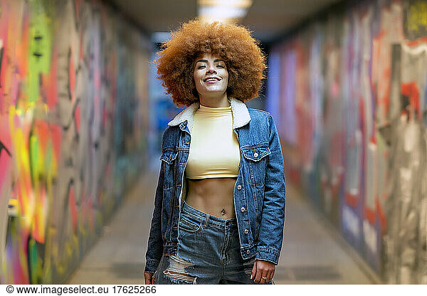 Smiling woman with Afro hairstyle standing by graffiti wall