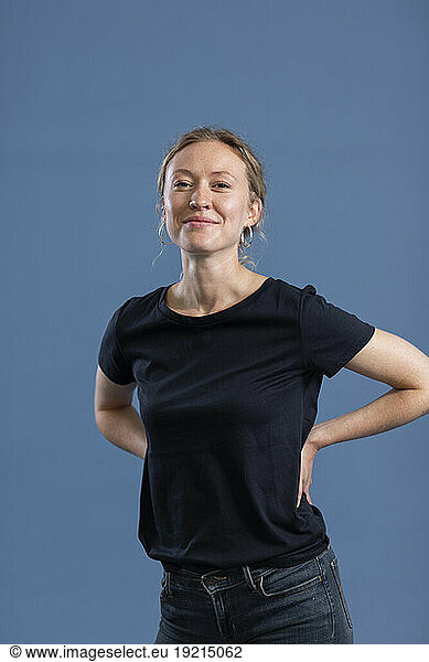 Smiling woman with arms akimbo standing against blue background