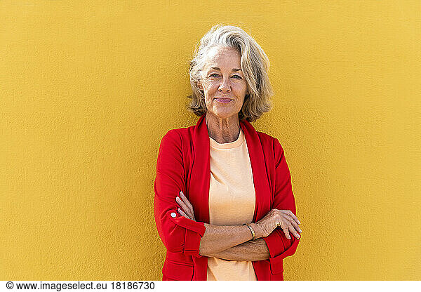 Smiling woman with arms crossed in front of yellow wall