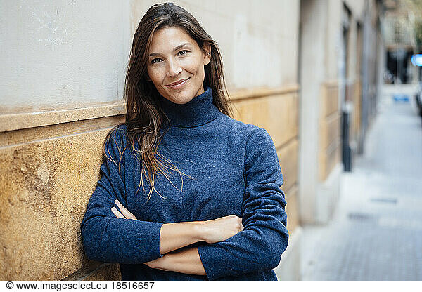 Smiling woman with arms crossed leaning on wall