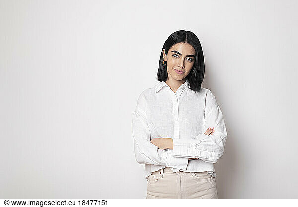 Smiling woman with arms crossed standing against white background