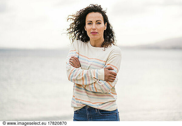 Smiling woman with arms crossed standing in front of sea