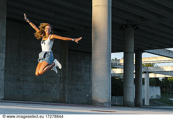 Smiling woman with arms outstretched enjoying while jumping at car park