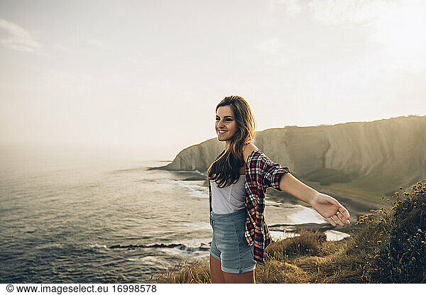 Smiling woman with arms outstretched looking at view while standing against sky