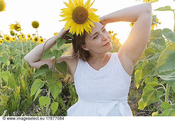 Smiling woman with arms raised holding sunflower on head