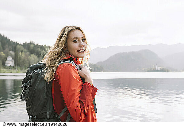 Smiling woman with backpack near lake