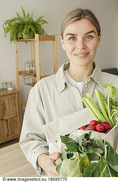 Smiling woman with bag of organic vegetables and fruits at home