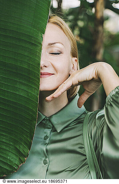 Smiling woman with banana leaf over face