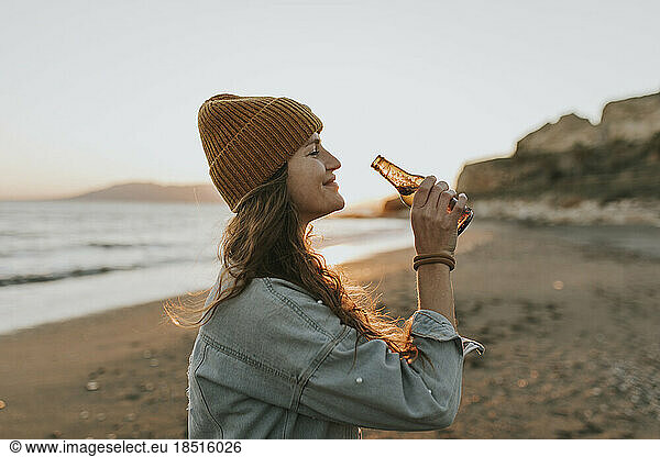 Smiling woman with beer bottle standing at beach