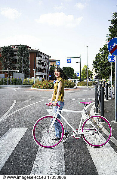 Smiling woman with bicycle standing on road