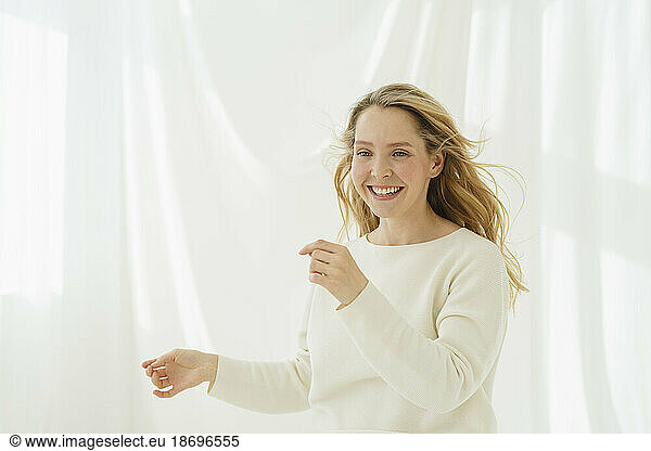 Smiling woman with blond hair dancing in front of white translucent curtain