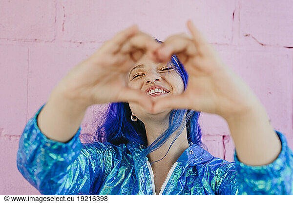 Smiling woman with blue dyed hair looking through heart shape