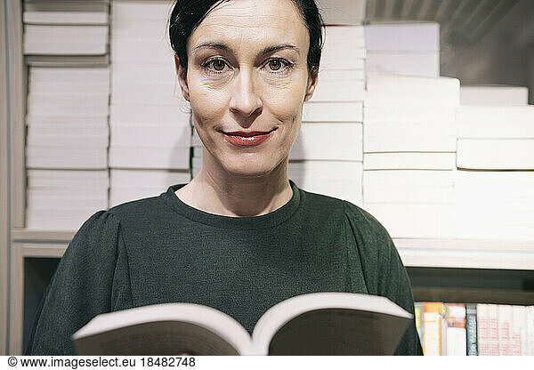 Smiling woman with book in front of bookshelf
