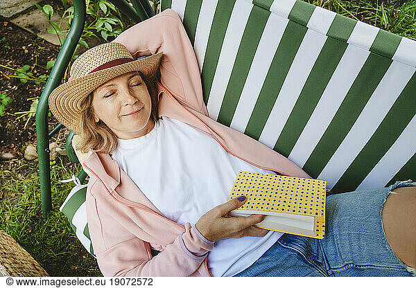 Smiling woman with book relaxing on green swing