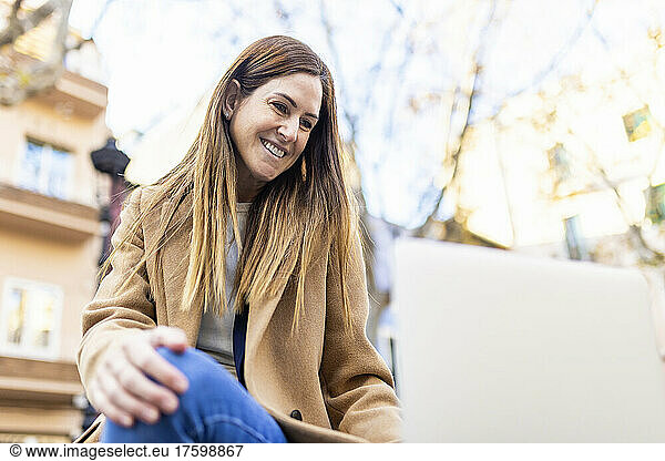 Smiling woman with brown hair looking at laptop in city