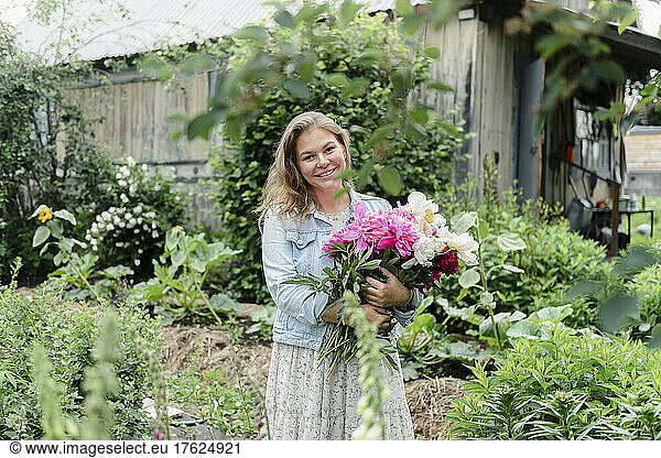 Smiling woman with bunch of flowers standing in garden