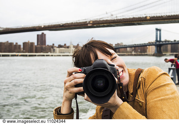Smiling woman with camera against Brooklyn bridge and East River