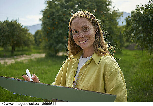 Smiling woman with cardboard cut out and felt tip pen in garden