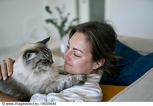 Smiling woman with cat lying on sofa at home