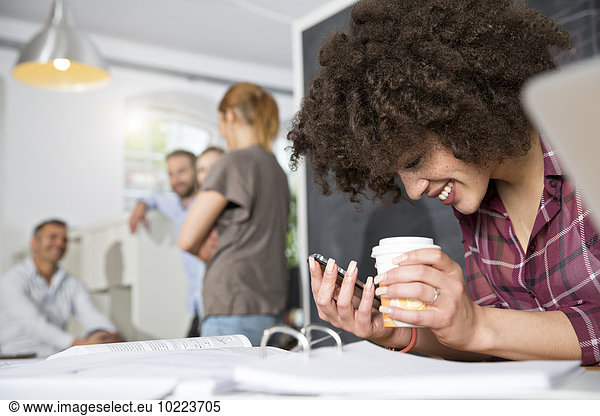 Smiling woman with cell phone and coffee to go in office