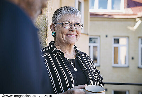Smiling woman with coffee cup by man in balcony